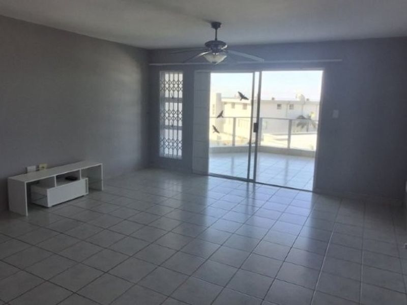 Spacious living area featuring neutral tiled flooring, a ceiling fan, and large sliding glass doors providing access to an outdoor balcony.