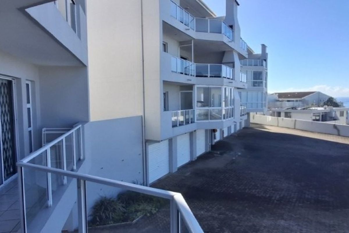 Exterior view of the apartment complex featuring glass balustrades, sliding doors, and a paved driveway area with garage access.