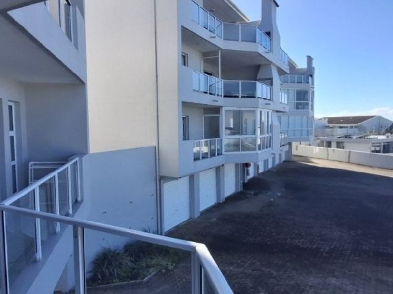 Exterior view of the apartment complex featuring glass balustrades, sliding doors, and a paved driveway area with garage access.