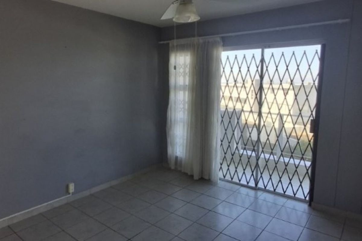 An empty bedroom featuring tiled flooring, a ceiling fan, and a sliding glass door with an integrated security gate leading to an outdoor area.