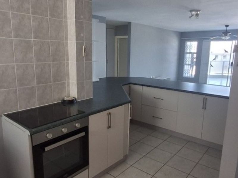 Open-plan kitchen featuring built-in cabinetry, electric hob, oven, and tiled splashback, flowing into a spacious living area with tiled flooring.