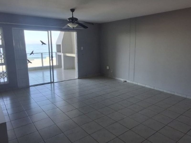 Spacious, empty living area featuring tiled flooring, a ceiling fan, and direct access to a balcony with ocean views.