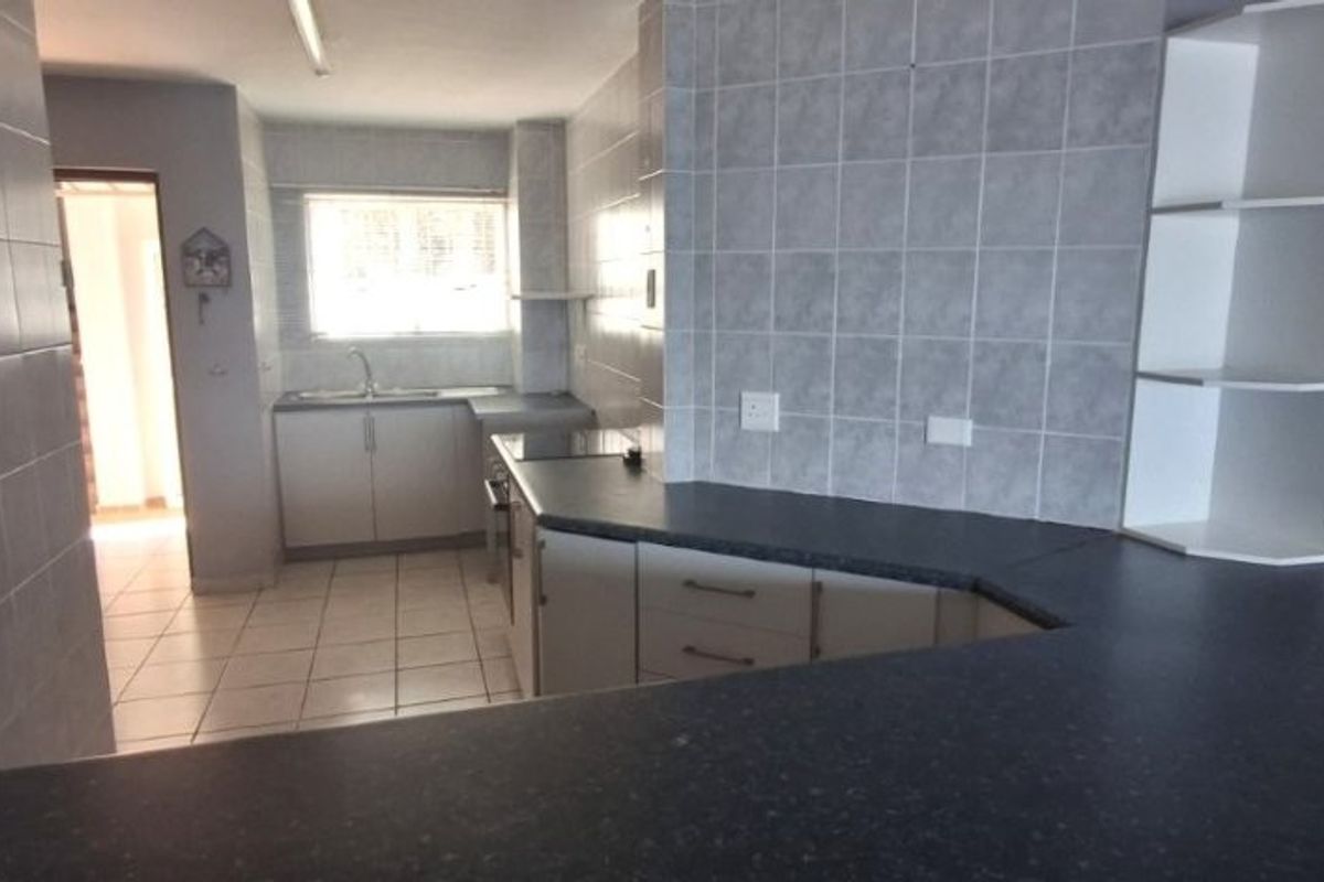 A functional kitchen featuring laminate countertops, tiled splashbacks, built-in cabinetry, and a stainless steel sink, presented in a clean, empty state.