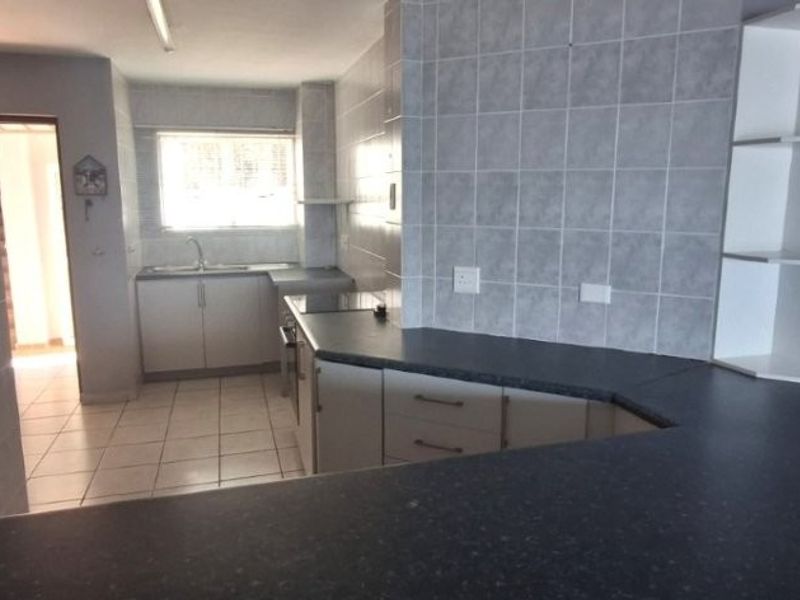 A functional kitchen featuring laminate countertops, tiled splashbacks, built-in cabinetry, and a stainless steel sink, presented in a clean, empty state.