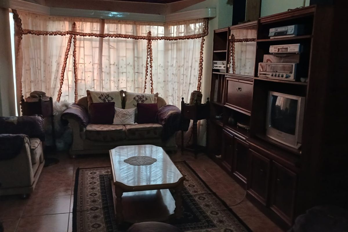 A living room featuring tiled flooring, a large bay window with curtains, and built-in wooden cabinetry.