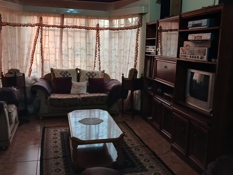 A living room featuring tiled flooring, a large bay window with curtains, and built-in wooden cabinetry.