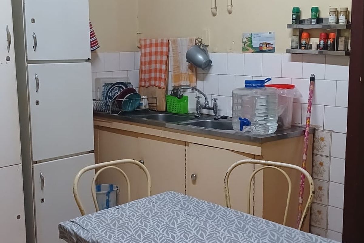 A compact kitchen area featuring tiled splashbacks, a stainless steel sink, and tiled flooring, requiring some cosmetic updates to the wall finishes.