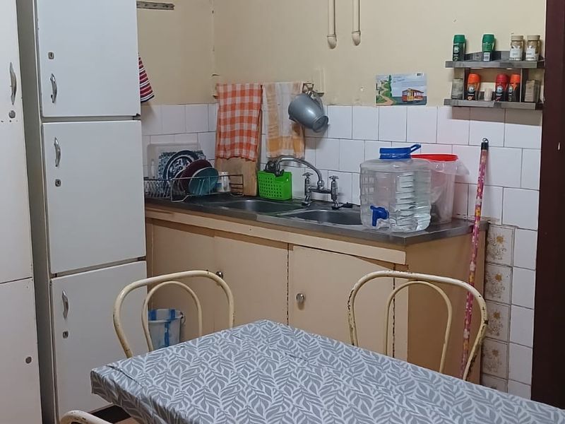 A compact kitchen area featuring tiled splashbacks, a stainless steel sink, and tiled flooring, requiring some cosmetic updates to the wall finishes.