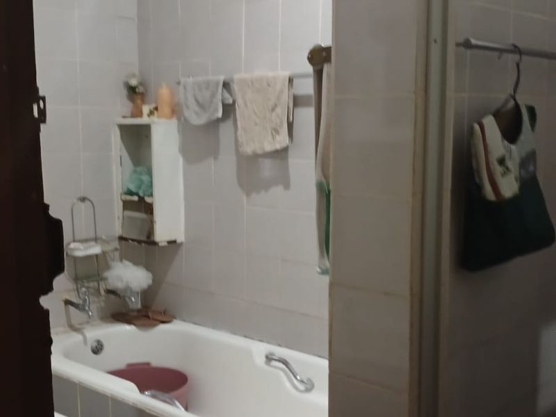 A functional bathroom featuring a bathtub, wall tiling, and a built-in basin, currently showing signs of age and wear.