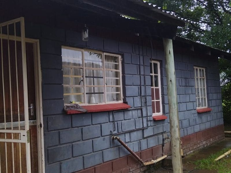 Rear exterior view of a house featuring painted concrete block walls, steel security gates, and a corrugated metal roof structure.