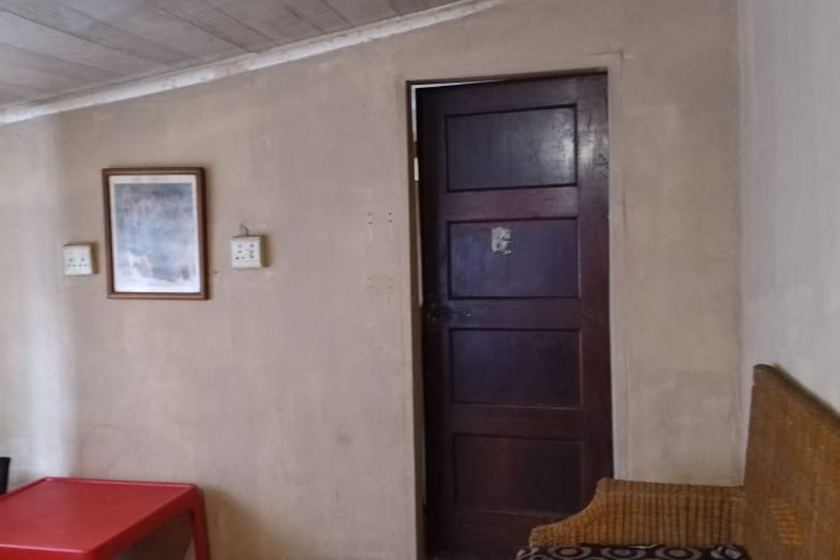 A living area featuring a timber ceiling and a solid timber door, requiring cosmetic updates to the wall finishes and overall interior presentation.