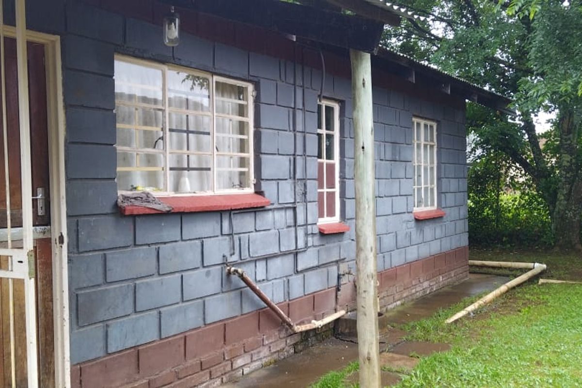 Rear exterior view of a concrete block house featuring security gates, steel windows with burglar bars, and exposed exterior plumbing.