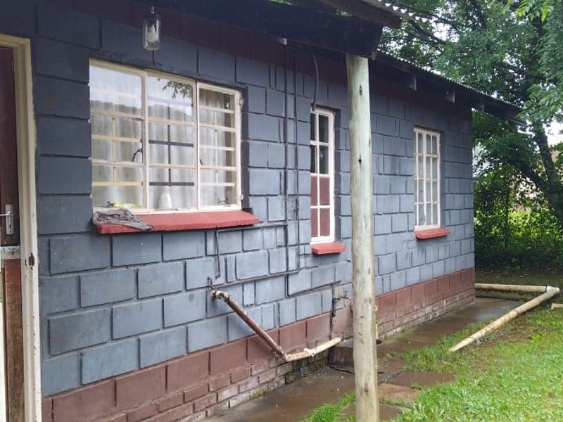 Rear exterior view of a concrete block house featuring security gates, steel windows with burglar bars, and exposed exterior plumbing.