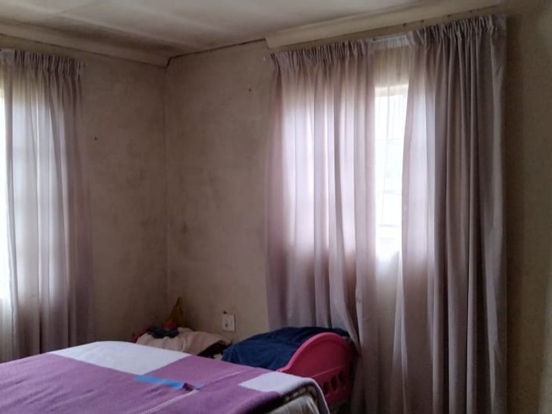 A bedroom featuring dual windows with curtains, requiring cosmetic updates to the wall finishes and ceiling to improve the overall condition.