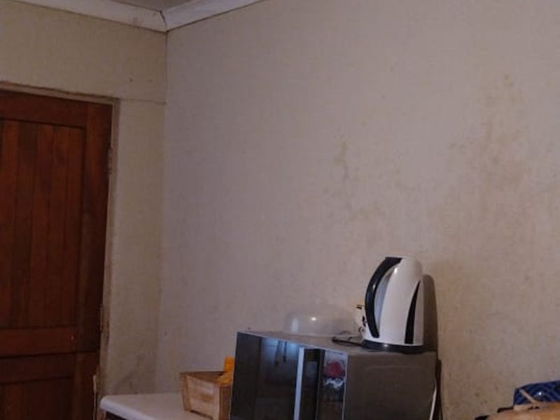 A dated kitchen area featuring built-in cabinetry and tiled flooring, showing visible signs of water damage on the walls and ceiling.
