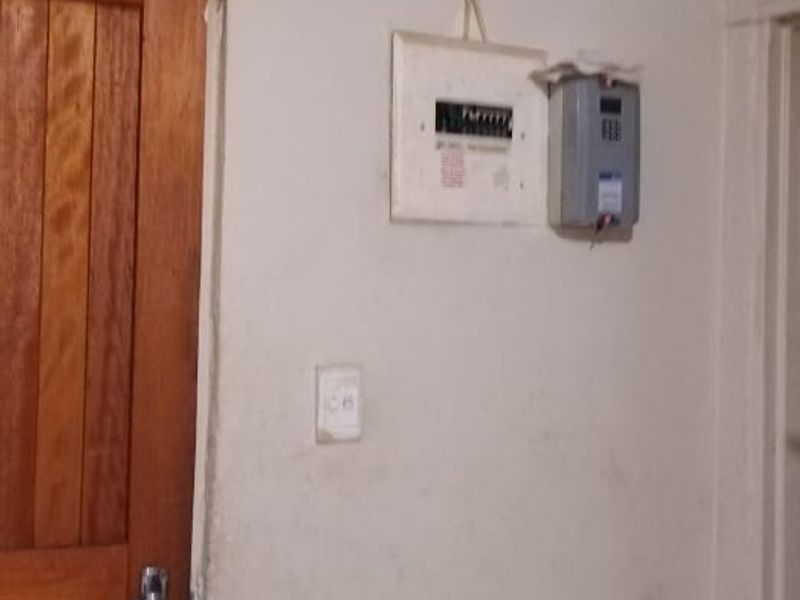 A hallway area featuring a timber door, electrical distribution board, and prepaid meter, showing signs of wear and surface damage to the walls.