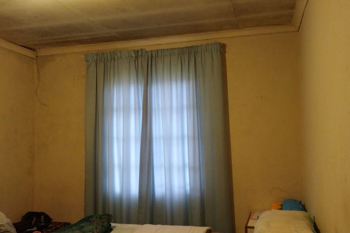 A bedroom featuring basic wall finishes and ceiling tiles, currently showing signs of wear and requiring cosmetic updates to improve the overall aesthetic.