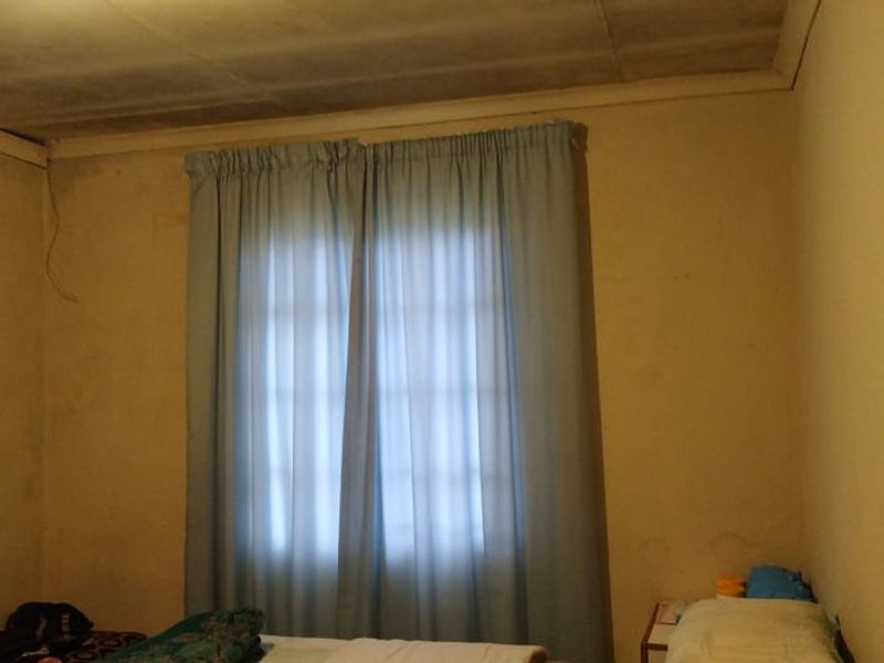 A bedroom featuring basic wall finishes and ceiling tiles, currently showing signs of wear and requiring cosmetic updates to improve the overall aesthetic.