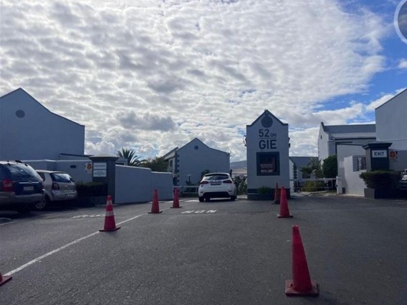 The entrance to the residential complex featuring a security gatehouse, boom gate access, and paved driveway.