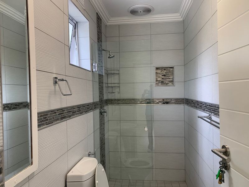 A modern, well-maintained bathroom featuring a glass-enclosed shower, tiled walls with decorative mosaic accents, and a built-in wall niche.