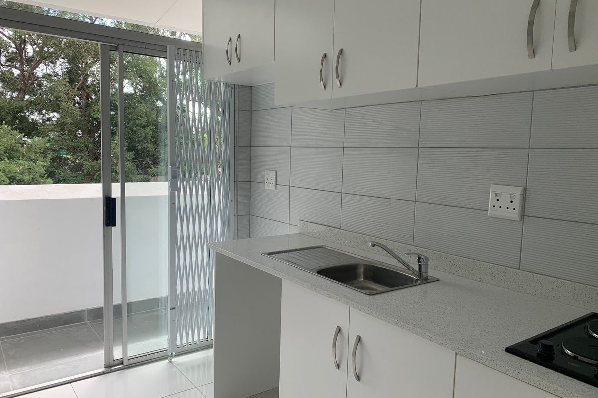 Modern kitchen featuring white cabinetry, stone countertops, stainless steel sink, and built-in hob, with direct access to a balcony through a sliding glass door.