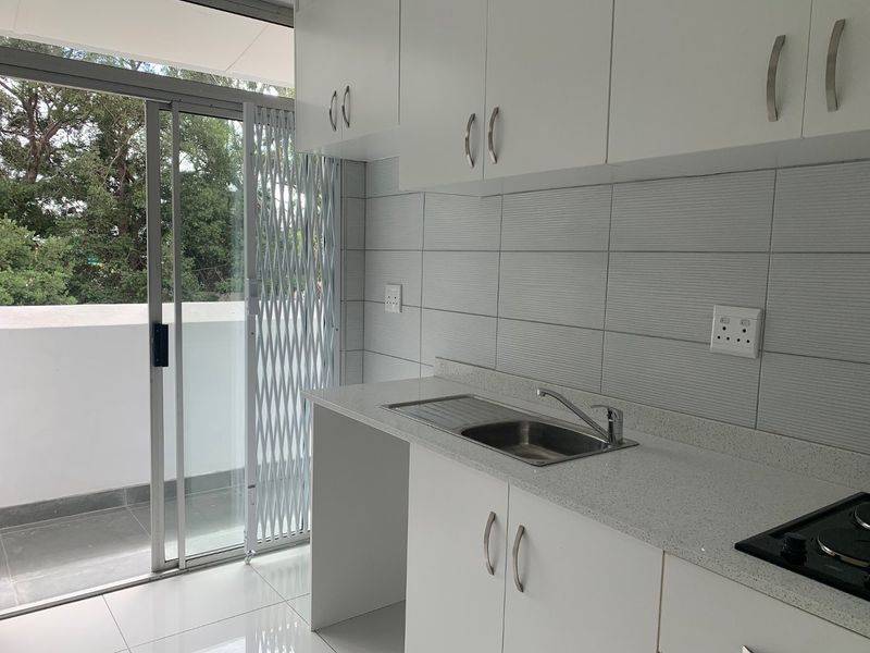 Modern kitchen featuring white cabinetry, stone countertops, stainless steel sink, and built-in hob, with direct access to a balcony through a sliding glass door.