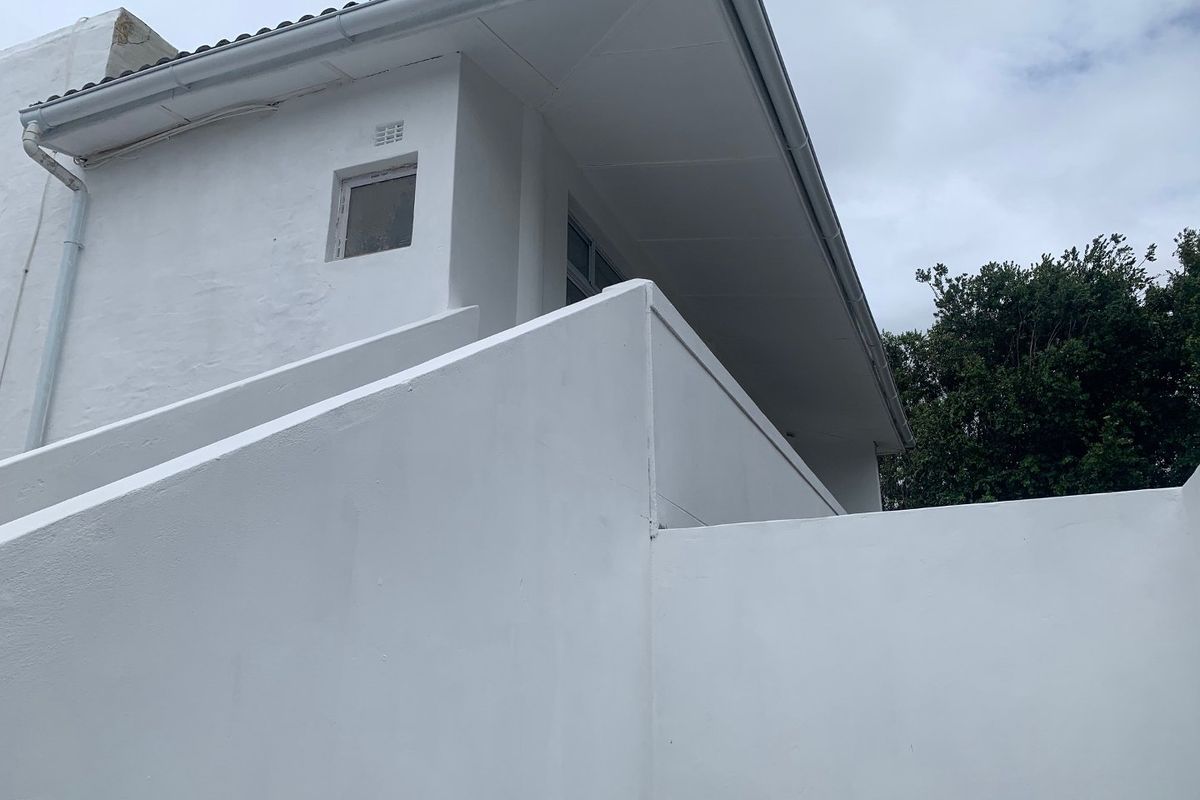A view of the exterior rear facade featuring white painted walls, roof eaves, and functional guttering systems.