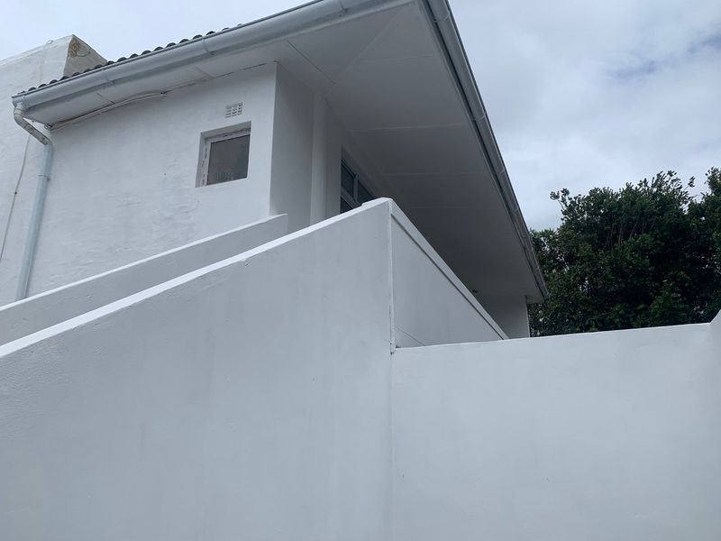 A view of the exterior rear facade featuring white painted walls, roof eaves, and functional guttering systems.