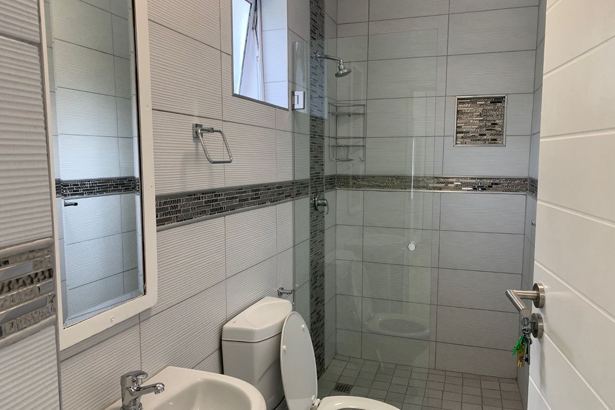 Modern bathroom featuring a walk-in shower with glass screen, mosaic tile accents, pedestal basin, and neutral ceramic wall tiling.