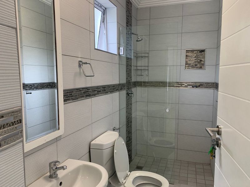 Modern bathroom featuring a walk-in shower with glass screen, mosaic tile accents, pedestal basin, and neutral ceramic wall tiling.