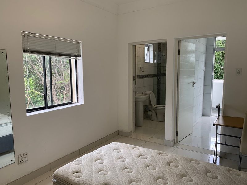 A bedroom featuring tiled flooring, an aluminium-framed window with blinds, and direct access to an en-suite bathroom.