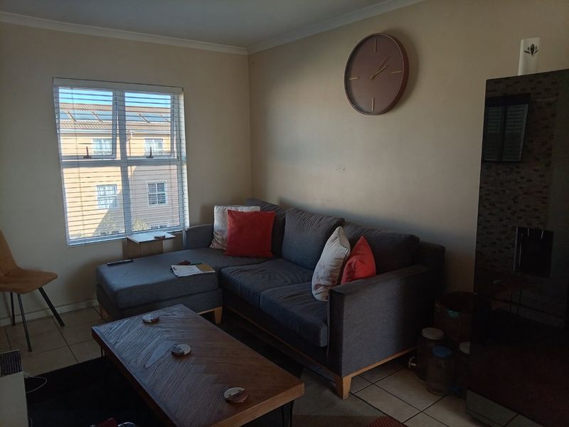 A living room featuring tiled flooring and a large window with blinds, providing natural light to the space.