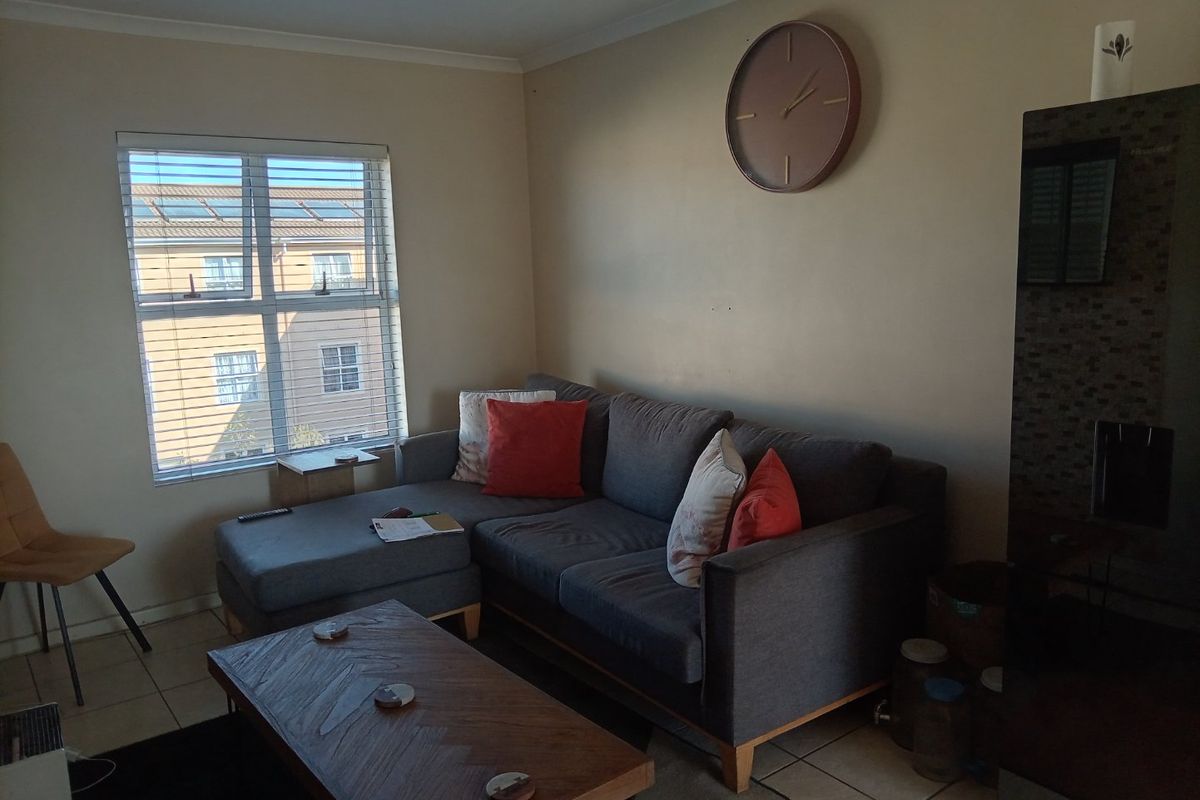 A comfortable living room featuring tiled flooring, neutral wall tones, and a large window with venetian blinds providing natural light.