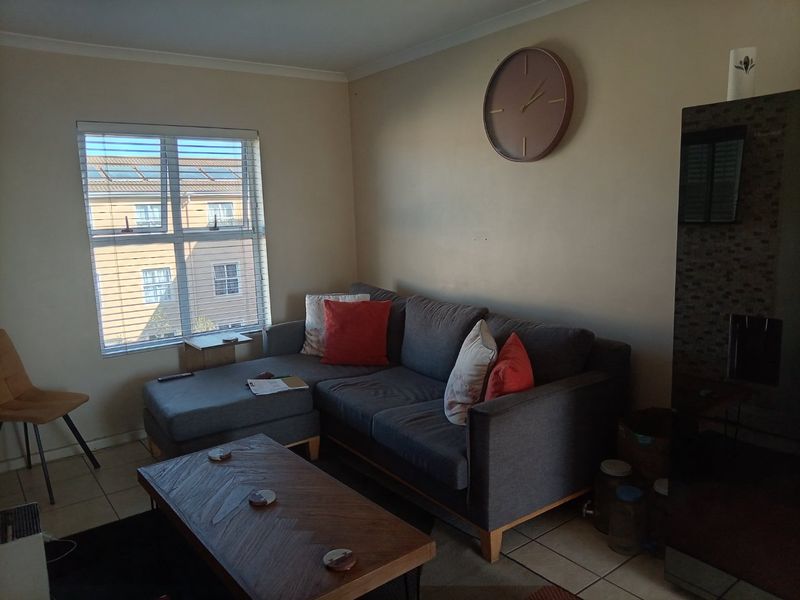 A comfortable living room featuring tiled flooring, neutral wall tones, and a large window with venetian blinds providing natural light.