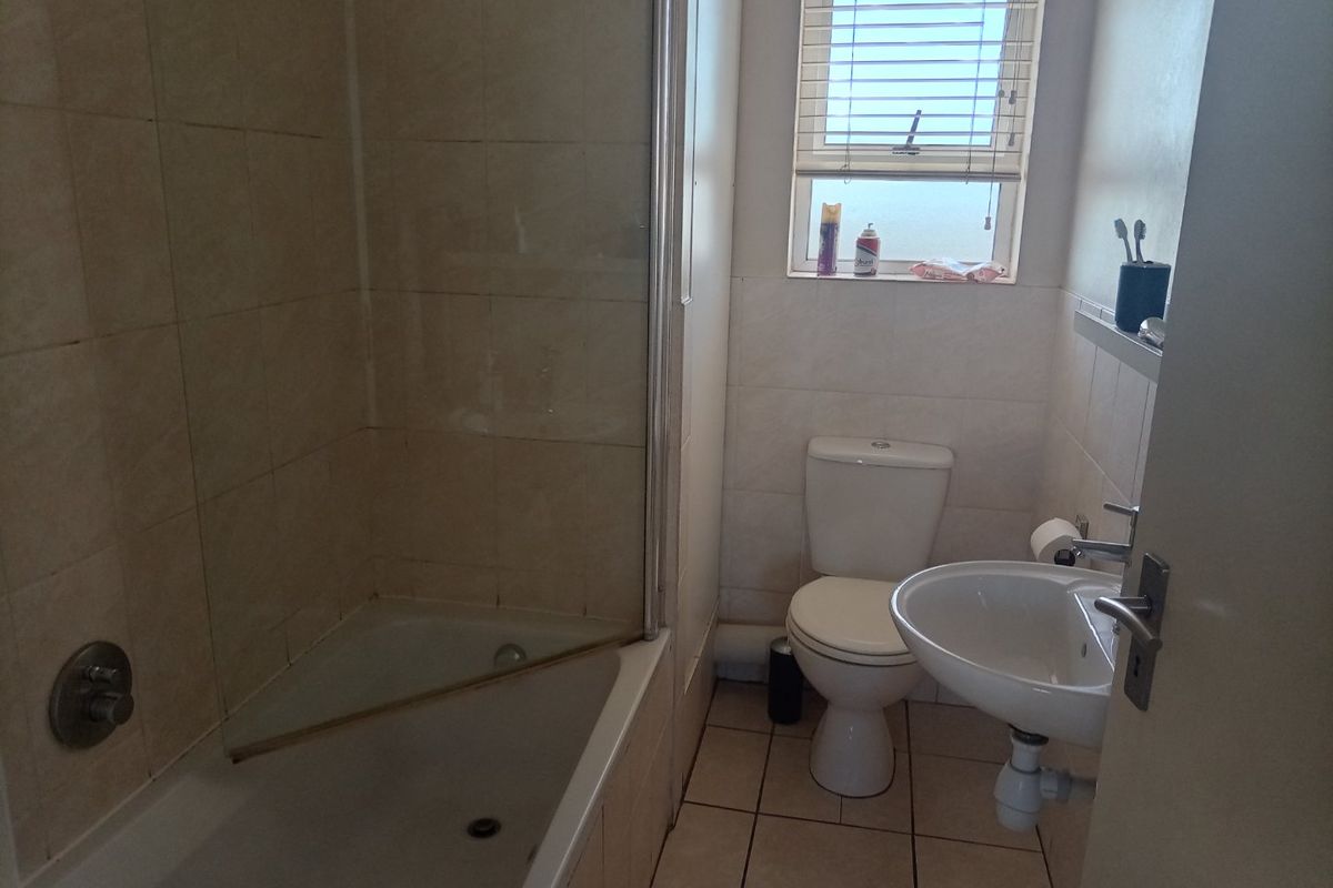 A functional bathroom featuring a bathtub with a glass shower screen, a pedestal sink, and a toilet, finished with neutral wall and floor tiles.