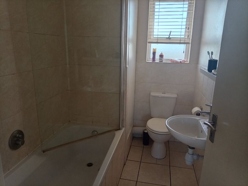 A functional bathroom featuring a bathtub with a glass shower screen, a pedestal sink, and a toilet, finished with neutral wall and floor tiles.