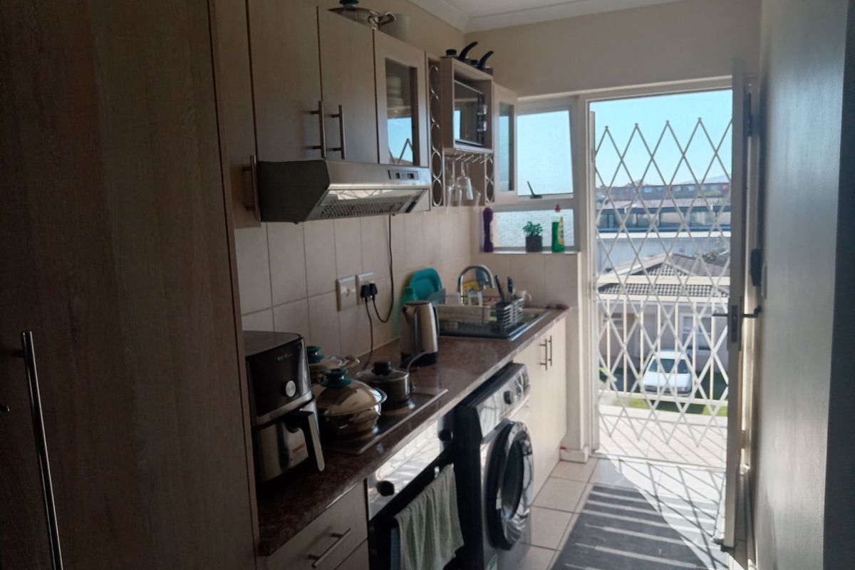 Compact kitchen featuring built-in cabinetry, integrated oven and hob, and direct access to an exterior area through a security gate.