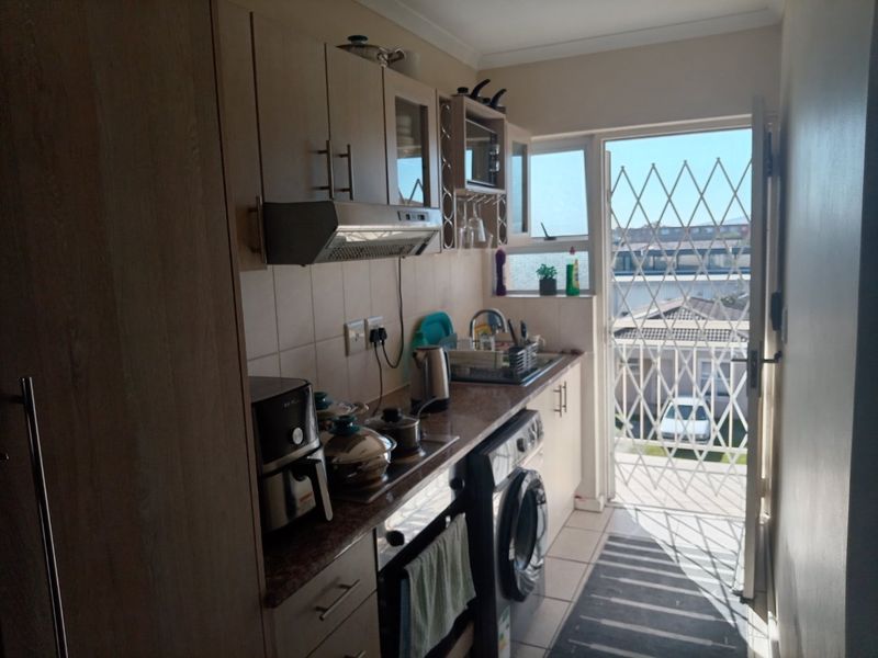 Compact kitchen featuring built-in cabinetry, integrated oven and hob, and direct access to an exterior area through a security gate.