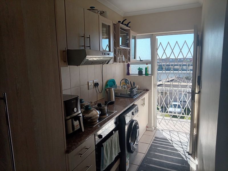 Compact scullery area featuring built-in cabinetry, laminate countertops, stainless steel sink, and direct access to the exterior via a security gate.