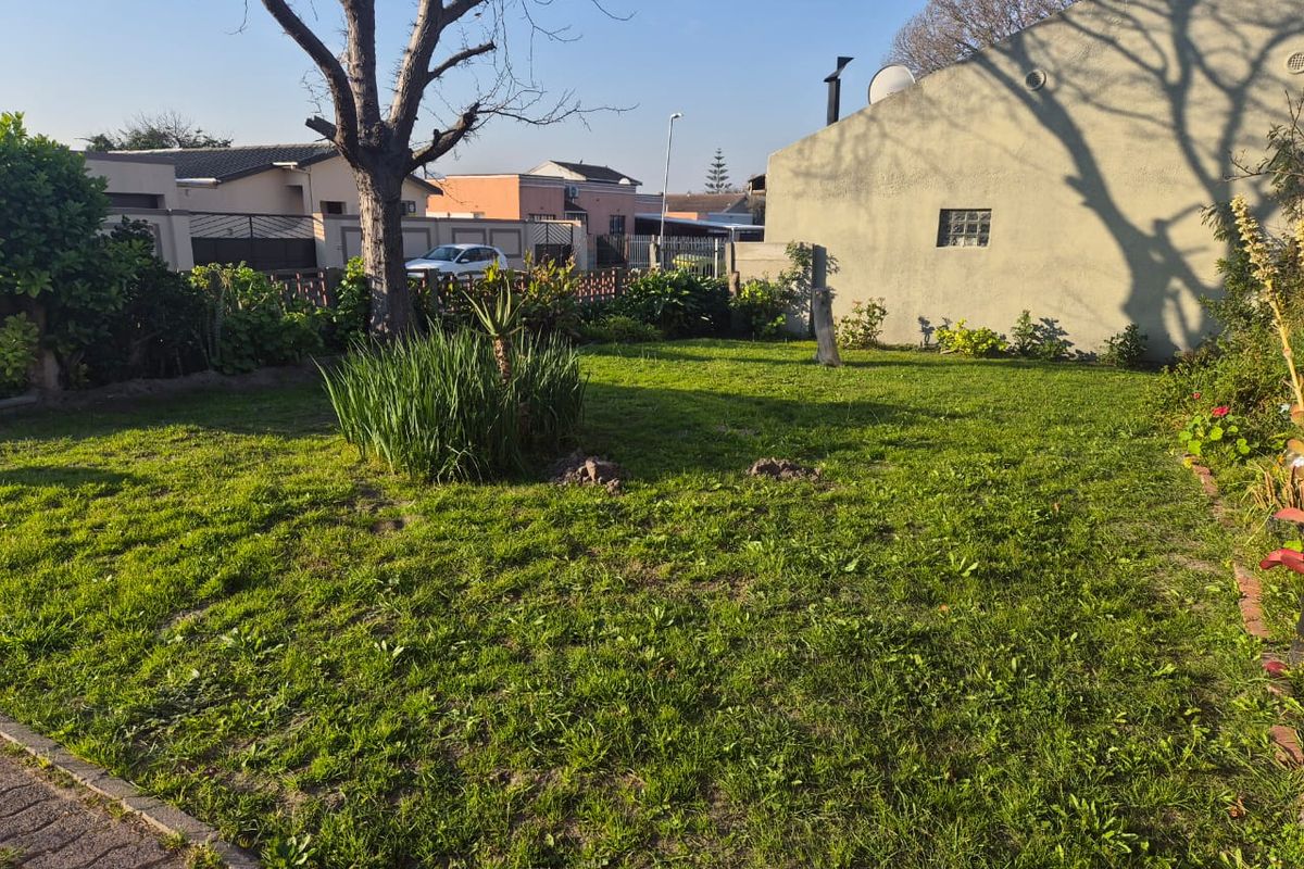 A spacious residential garden featuring a large lawn, mature tree, and boundary wall, providing a private outdoor space for the property.