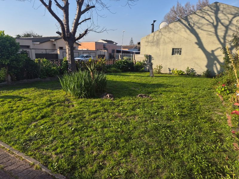 A spacious residential garden featuring a large lawn, mature tree, and boundary wall, providing a private outdoor space for the property.