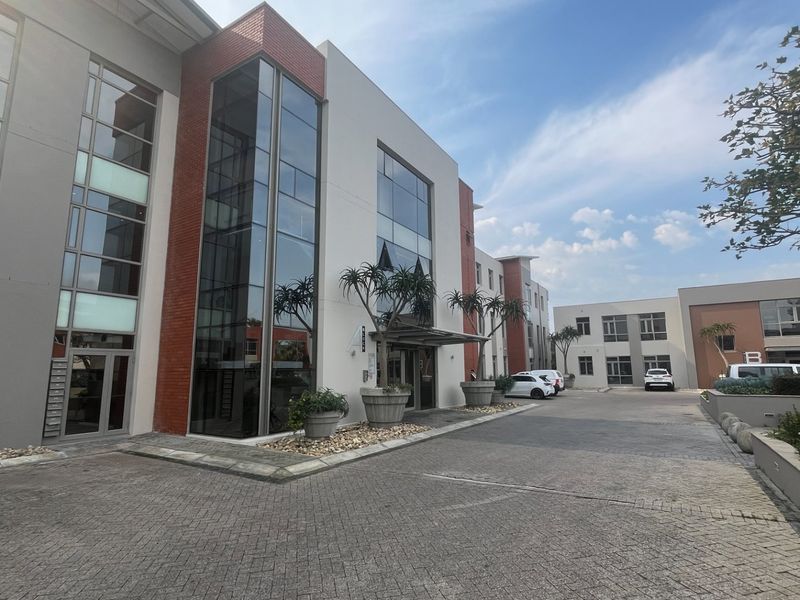 Modern commercial office building exterior featuring a paved driveway, glass facade, and brick accents with a professional entrance area.