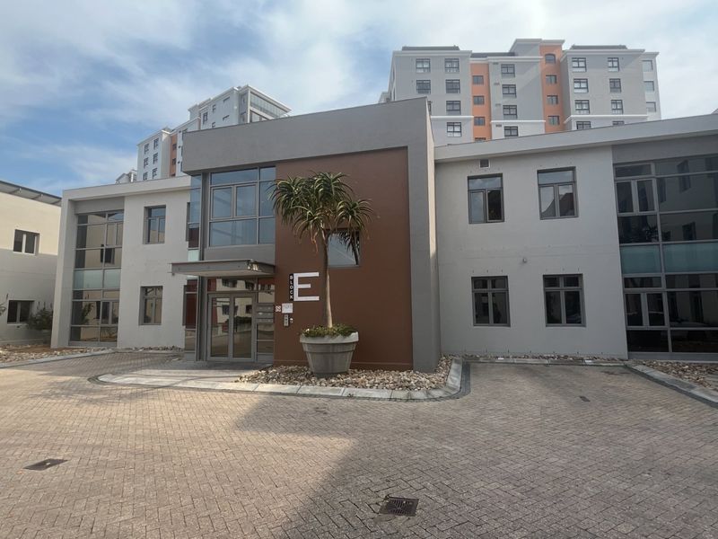 Modern commercial building facade featuring a paved entrance area, aluminium framed windows, and clear block identification signage.