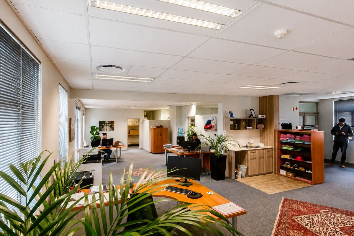 Open-plan commercial office space featuring suspended ceilings, recessed lighting, carpeted flooring, and a small built-in kitchenette area.