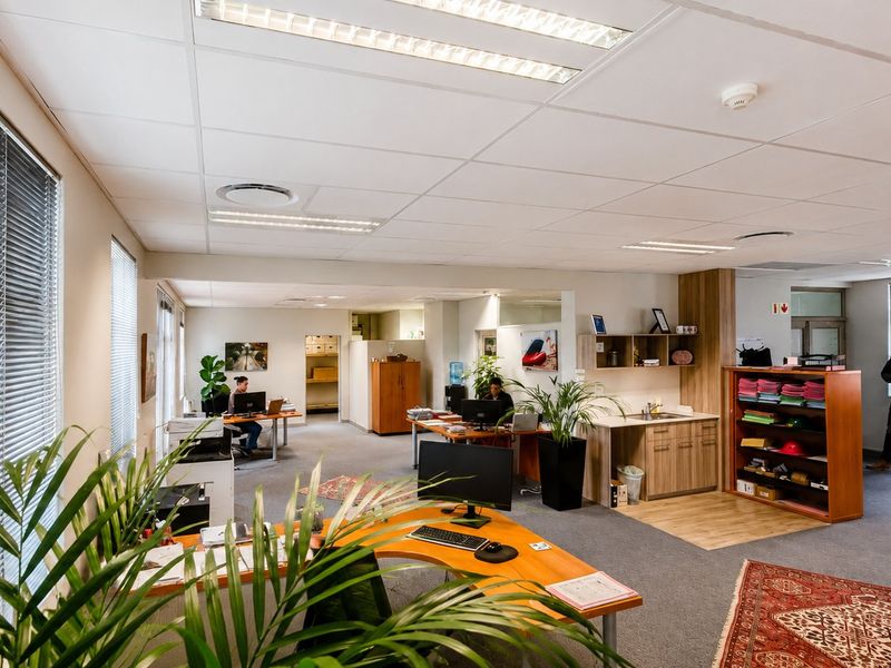 Open-plan commercial office space featuring suspended ceilings, recessed lighting, carpeted flooring, and a small built-in kitchenette area.