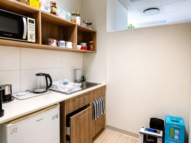 A functional commercial scullery or kitchenette area featuring built-in cabinetry, a stainless steel sink, tiled backsplash, and integrated microwave space.