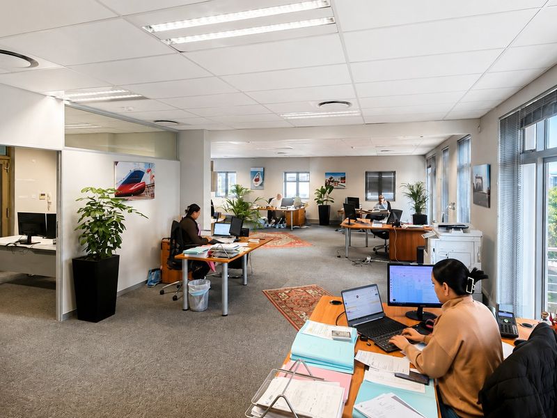 A spacious, open-plan commercial office featuring large windows with venetian blinds, suspended ceilings with recessed lighting, and carpeted flooring.