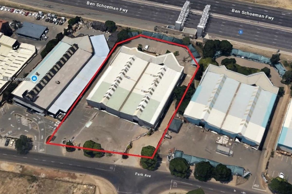 Aerial view of an industrial warehouse property featuring a large metal roof, skylights, and an asphalt parking area with perimeter fencing.