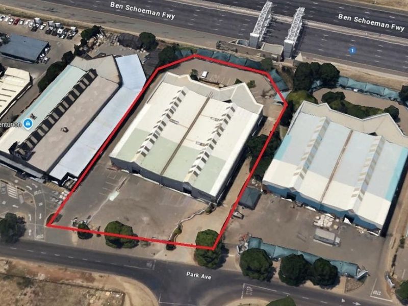 Aerial view of an industrial warehouse property featuring a large metal roof, skylights, and an asphalt parking area with perimeter fencing.