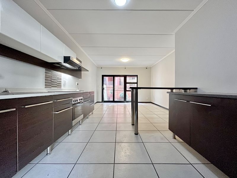 An open-plan kitchen and living area featuring modern dark cabinetry, a breakfast bar, tiled flooring, and a sliding door leading to the exterior.
